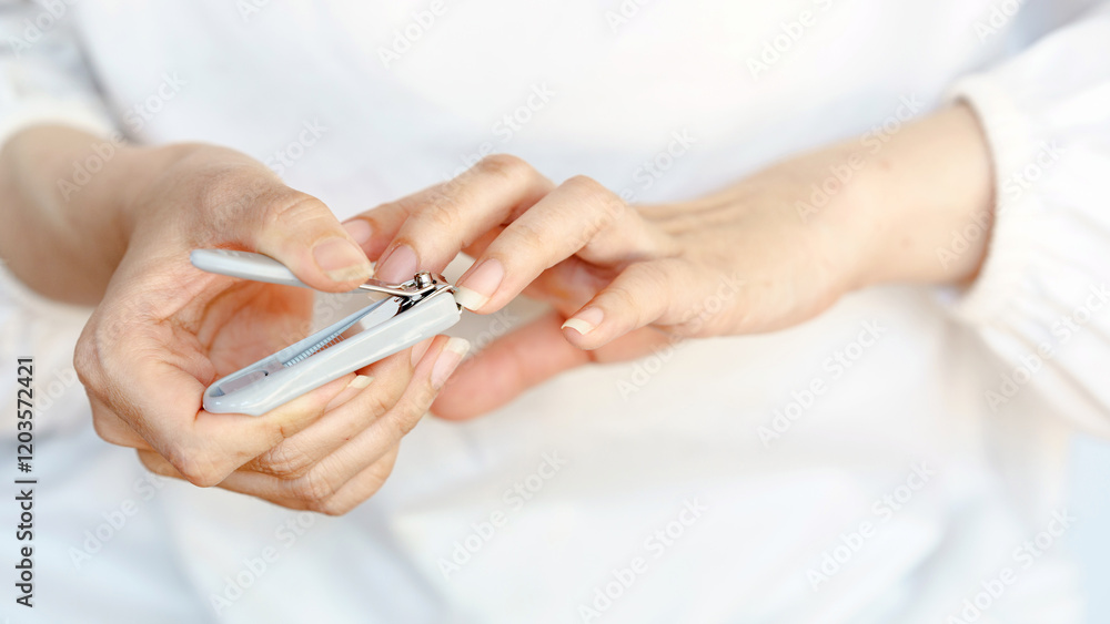 Close-up of hands using nail clippers to trim fingernails, emphasizing personal hygiene and grooming on a neutral background. Close-up of hands using nail clippers to trim fingernails, emphasizing personal hygiene and grooming on a neutral background.