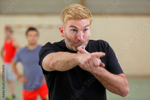 angry referee blowing a whistle and pointing with his hand photo