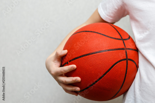 Teenage boy in white T-shirt holding orange basketball under his arm.