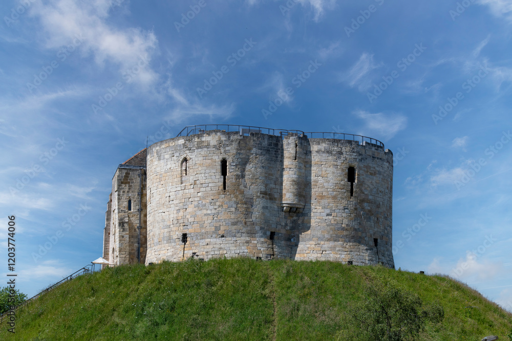 Low angle view of York Castle a ruined keep or fortification of medieval Norman castle or Clifford's Tower in the city of York, England against a white clouded blue sky Low angle view of York Castle a ruined keep or fortification of medieval Norman castle or Clifford's Tower in the city of York, England against a white clouded blue sky