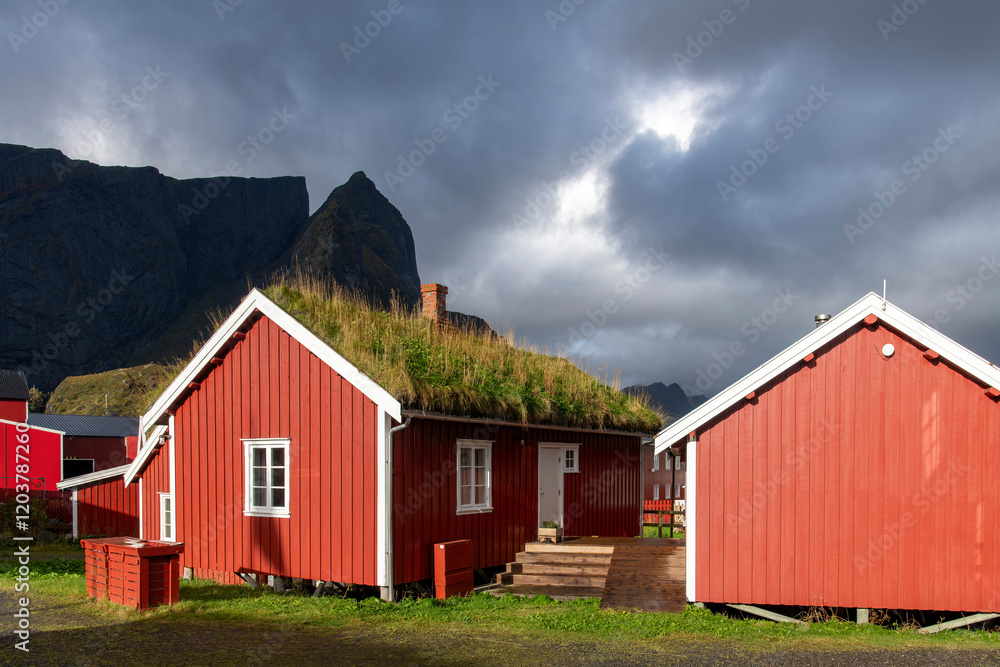 Close up of typical red (fisherman) cabin (rorbu) with sod roof in Reine, Norway on Lofoten island chain archipelago with mountains and dark clouds in the background Close up of typical red (fisherman) cabin (rorbu) with sod roof in Reine, Norway on Lofoten island chain archipelago with mountains and dark clouds in the background