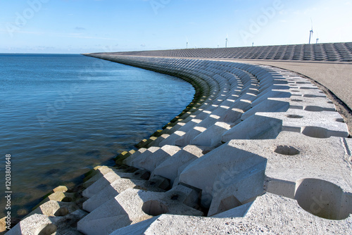 Curved dike body with concrete blocks near port of escape on former Breezand working island on Afsluitdijk (dam separates IJsselmeer lake from Wadden Sea), the Netherlands against a clear blue sky