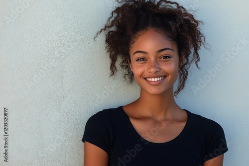 Beautiful young woman smiling while leaning against a wall in a serene outdoo...