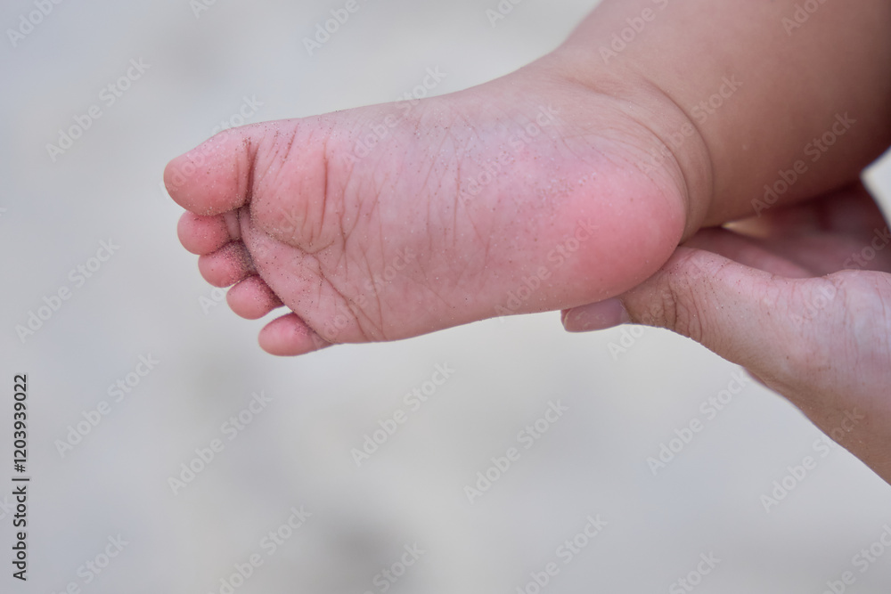 someone holding a baby ' s foot with a small piece of sand in the background someone holding a baby ' s foot with a small piece of sand in the background