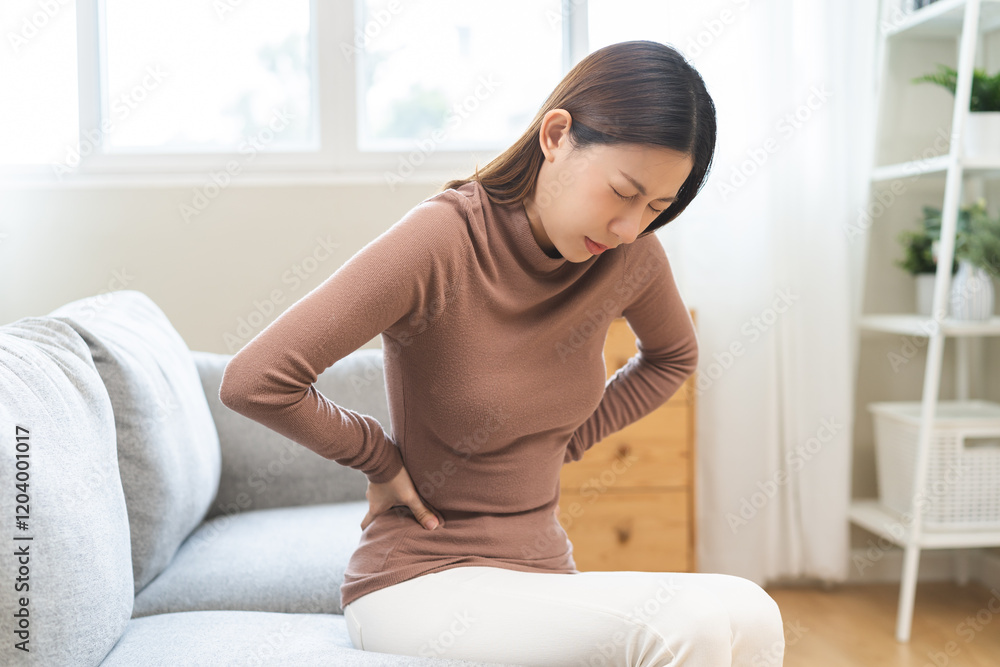 Pain body muscles stiff problem, suffer asian young woman painful back, symptom injury ache from long study work, hand holding massaging or rubbing lower back hurt, sore sitting on sofa at home. Pain body muscles stiff problem, suffer asian young woman painful back, symptom injury ache from long study work, hand holding massaging or rubbing lower back hurt, sore sitting on sofa at home.