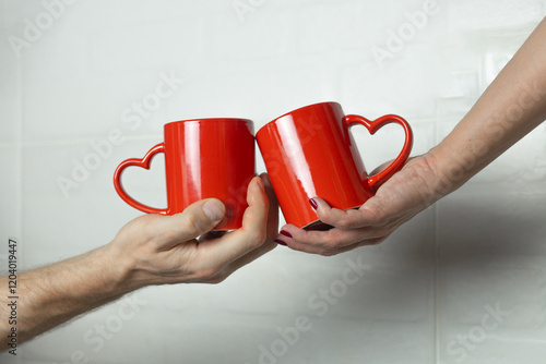 Obraz na plátne male and female hands holding red cups with handles in the form of hearts, love