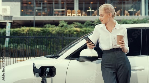 Wallpaper Mural Progressive businesswoman leaning on electric car and charging station before driving around city center. Eco friendly rechargeable EV car powered by sustainable and clean energy. Torontodigital.ca