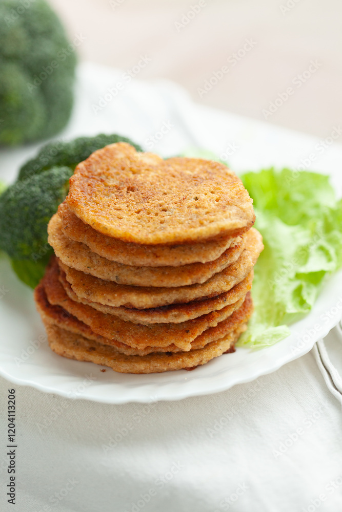 A stack of savory pancakes, golden brown and crispy, served on a white plate with fresh broccoli and lettuce. A stack of savory pancakes, golden brown and crispy, served on a white plate with fresh broccoli and lettuce.
