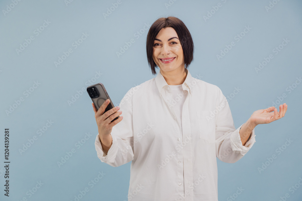 Smiling mature woman showing smartphone and gesturing on blue background Smiling mature woman showing smartphone and gesturing on blue background