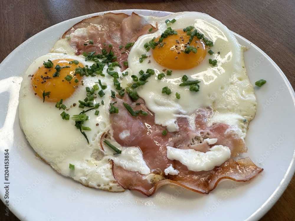 Sunny side up eggs with ham and chives on white plate Sunny side up eggs with ham and chives on white plate