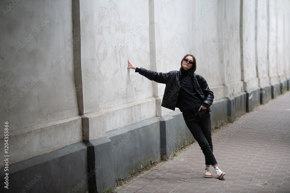 A person stands confidently against a weathered wall in an urban area, showcasing chic fashion and a relaxed pose while enjoying the sunlight in a lively neighborhood A person stands confidently against a weathered wall in an urban area, showcasing chic fashion and a relaxed pose while enjoying the sunlight in a lively neighborhood