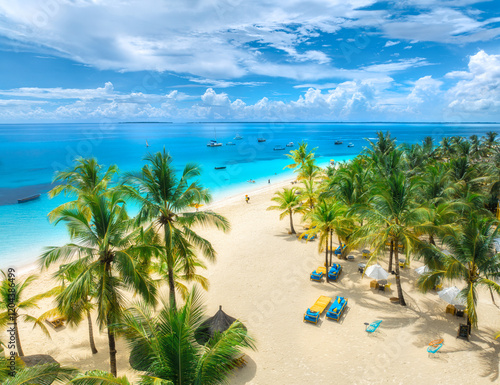 Fototapeta Naklejka Na Ścianę i Meble -  Aerial view of white sandy beach with palm trees, sunbeds, umbrellas, yachts, boats, blue ocean, sky with clouds at sunset. Summer in Kendwa, Zanzibar island. Tropical landscape. Clear sea. Top view