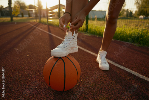 Female basketball player tying shoelaces putting foot on ball photo