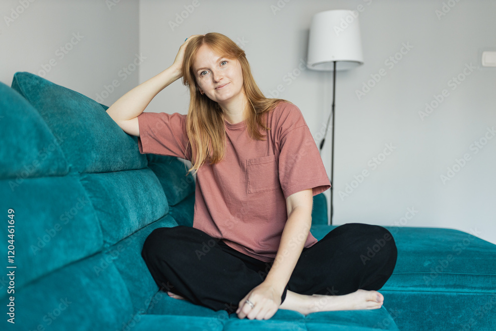 Young smiling happy woman wear casual clothes, looking camera siting on the sofa. People lounge concept. 30s female rest and spend free spare time in living room indoors