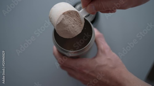 Muscular athlete using scoop to pour protein powder into shaker bottle, preparing nutritious post-workout supplement or meal replacement for optimal recovery and muscle gain. Shooting in slow motion.