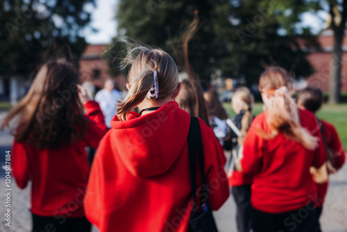 Fototapeta Naklejka Na Ścianę i Meble -  Group of school pupils and students on outdoor excursion tour in the city streets with guide, a docent with a tourist young visitors wearing red, school field trip, urban tour in the summer sunny day