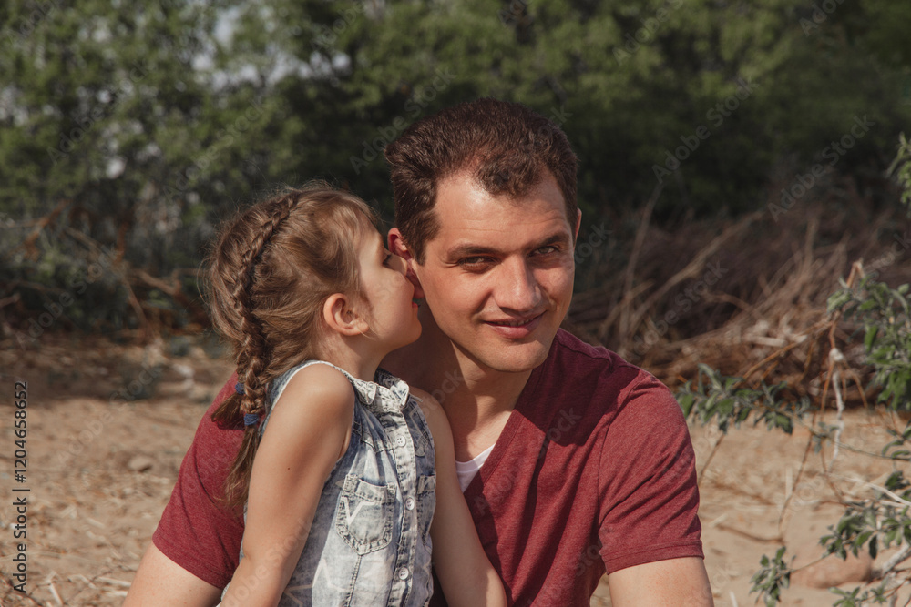Fototapeta premium little happy daughter whispering in smiling daddy's ear on sunny day