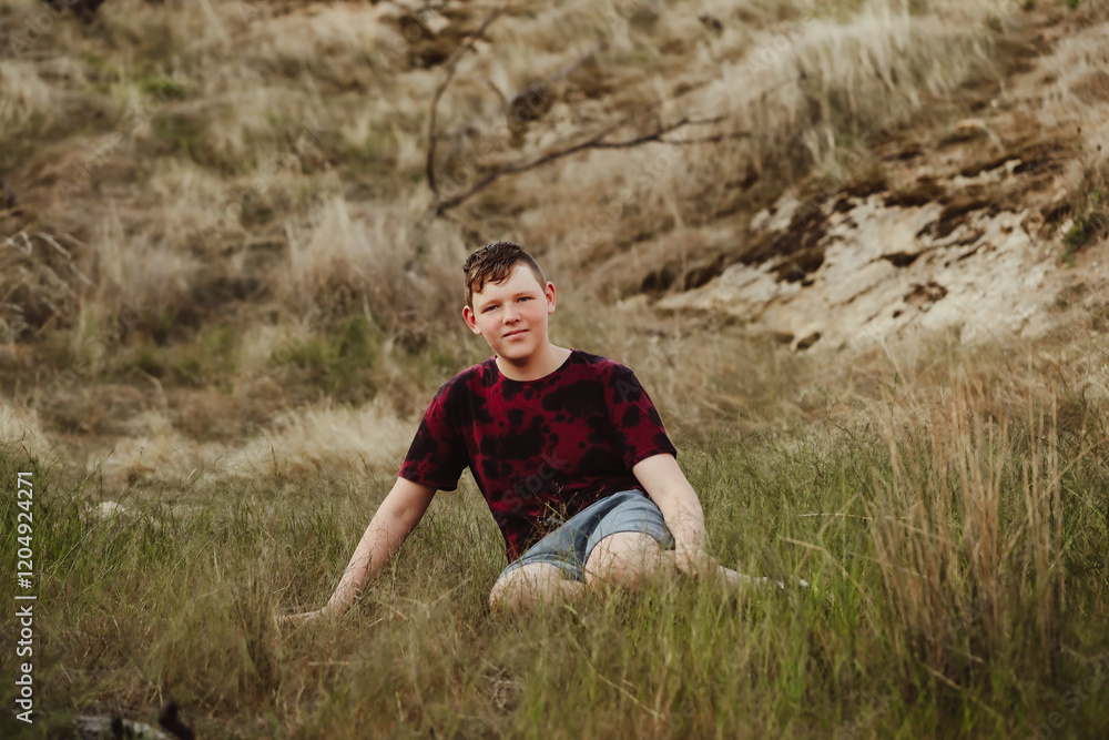Fototapeta premium Adolescent boy sitting in grass in the Australian bush