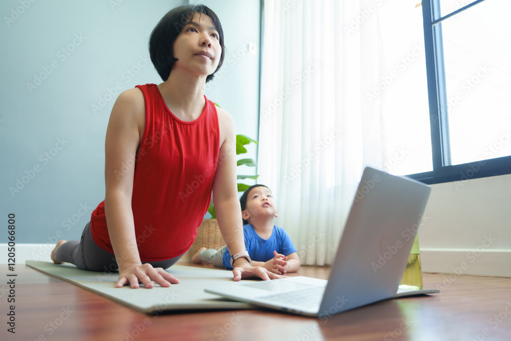 Obraz premium Asian Mother in red sportswear performing yoga on a mat with her young son, both following along with a laptop