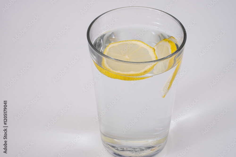 A refreshing glass of water with floating lemon slices on a white background. A refreshing glass of water with floating lemon slices on a white background.
