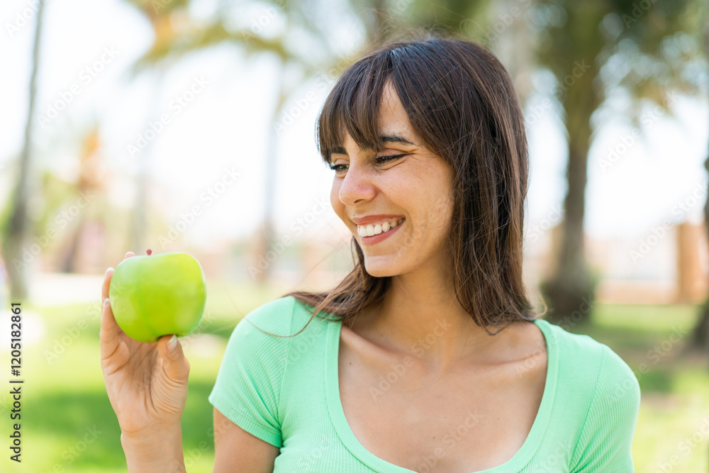 Young woman with an apple at outdoors with happy expression Young woman with an apple at outdoors with happy expression