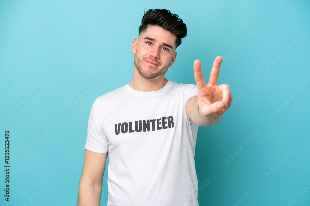 Young volunteer caucasian man isolated on blue background smiling and showing victory sign Young volunteer caucasian man isolated on blue background smiling and showing victory sign