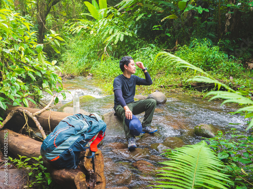 Solo hiker takes a break on rock in stream in the lush rainforest at Phu Soi Dao National Park, Thailand. photo