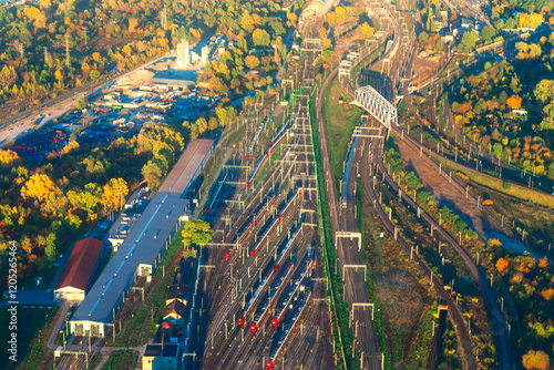 Obraz na płótnie Aerial view of bustling railway hub surrounded by vibrant autumn foliage, showcasing multiple tracks, trains, and industrial buildings. Perfect for themes of transportation, logistics, infrastructure w salonie