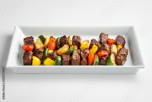 Grilled beef and vegetable skewers on a white rectangular platter. photo