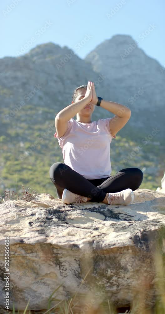 Vertical video: Meditating in nature, woman sitting cross-legged on rock during mountain hike Vertical video: Meditating in nature, woman sitting cross-legged on rock during mountain hike