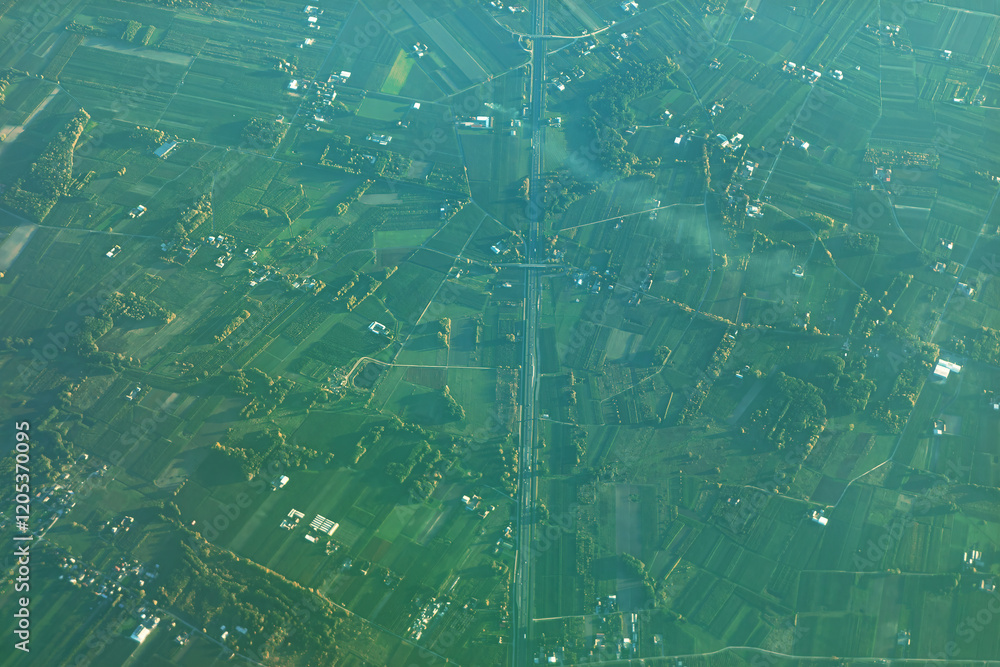 Captivating aerial view of a rural landscape with a central straight road dividing agricultural fields into geometric shapes, offering a striking look at land use patterns and rural planning