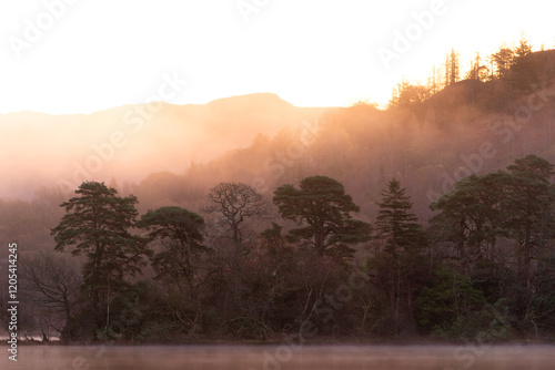 Dramatic atmospheric dawn landscape at Rydal Water in Lake District during Autumn with moody glow over mist on lake photo