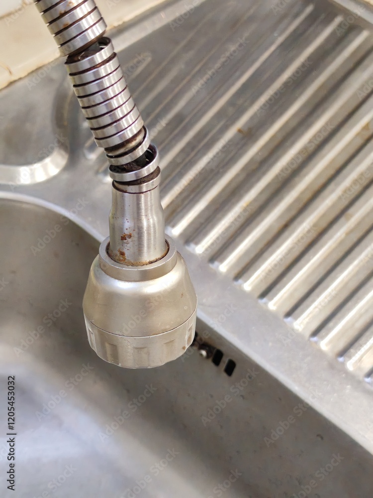 A detailed shot of a worn and rusting flexible faucet hose in a domestic stainless steel kitchen sink. Ideal for plumbing repair advertisements, home maintenance services or cleaning product promotion A detailed shot of a worn and rusting flexible faucet hose in a domestic stainless steel kitchen sink. Ideal for plumbing repair advertisements, home maintenance services or cleaning product promotion