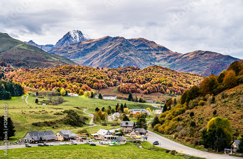 A picturesque cycling hub near Col d’Aspin, surrounded by rolling hills, autumn foliage, and majestic Pyrenean peaks, offering rest facilities, bike rentals, and vibrant outdoor activities.