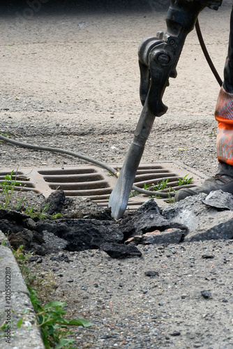 Industrial Worker Using Jackhammer on Concrete Surface Near a Drain Grate