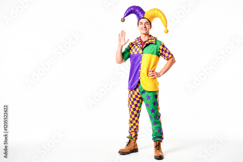 Cheerful young man in vibrant jester costume waving energetically in a bright studio, celebrating Mardi Gras Carnival spirit.