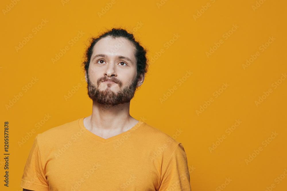 Fototapeta premium Male model with beard and bun hairstyle smiling against a bright yellow background, wearing a casual orange T shirt, evoking a positive and cheerful mood
