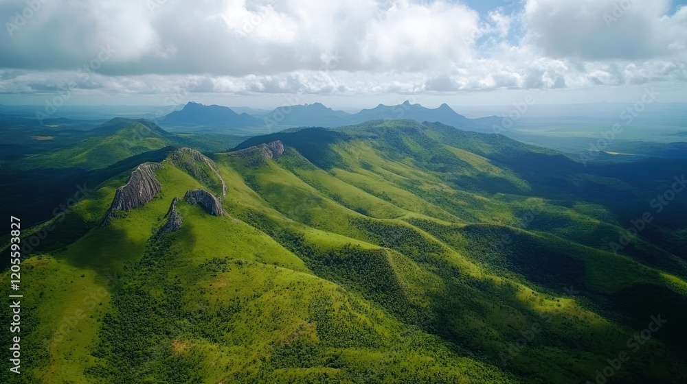 Obraz premium Aerial view of rolling green hills with rocky outcroppings under a cloudy sky