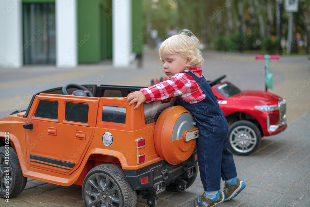 Cute happy blond little young toddler kid boy driving,riding in electric red toy car, automobile in park.Children physical, emotional development, childhood daycare, kindergarten concept. Cute happy blond little young toddler kid boy driving,riding in electric red toy car, automobile in park.Children physical, emotional development, childhood daycare, kindergarten concept.