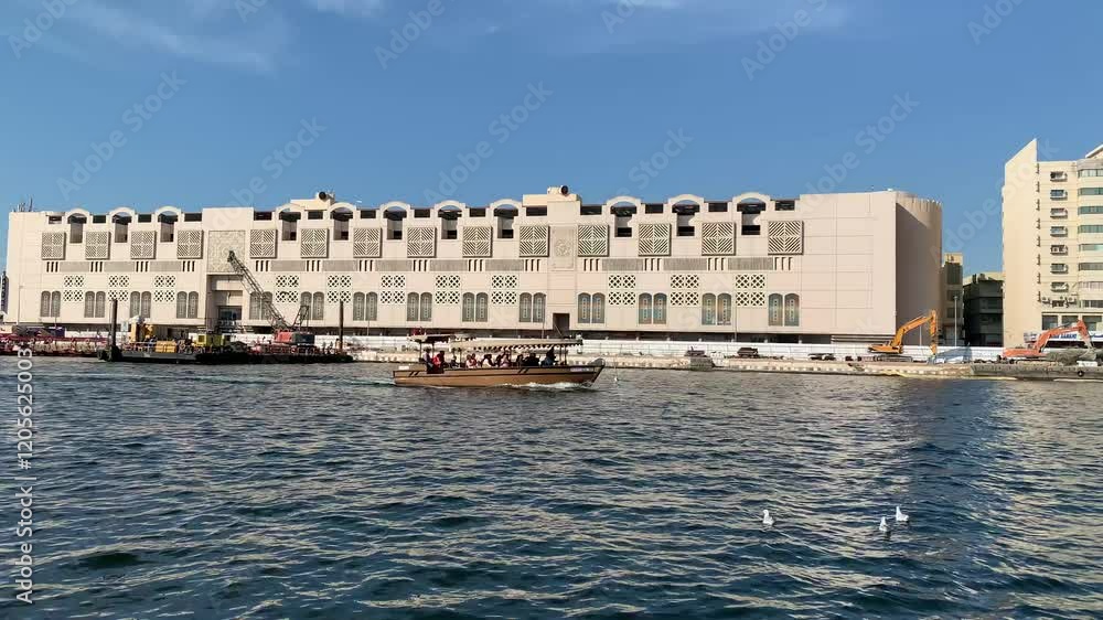 Traditional boat sails through Dubai creek. Motion of water. Deira Old Souk ferry station in the background. View from a boat. Dubai, United Arab Emirates Traditional boat sails through Dubai creek. Motion of water. Deira Old Souk ferry station in the background. View from a boat. Dubai, United Arab Emirates