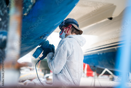 a man polishing the side of the hull of a blue ship.