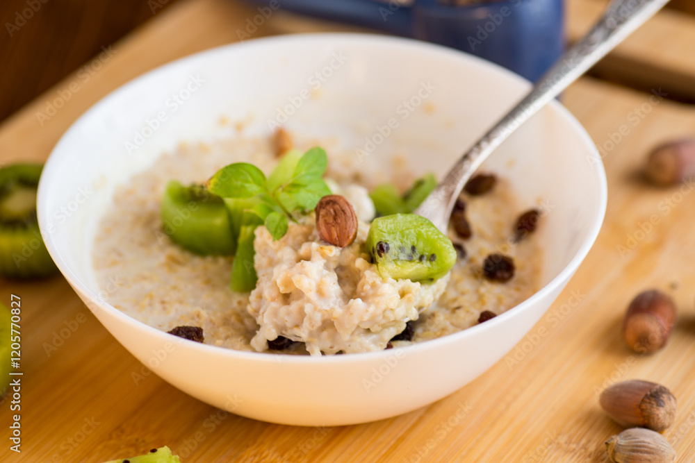 cooked oatmeal with kiwi, honey and nuts in a bowl on a wooden table cooked oatmeal with kiwi, honey and nuts in a bowl on a wooden table