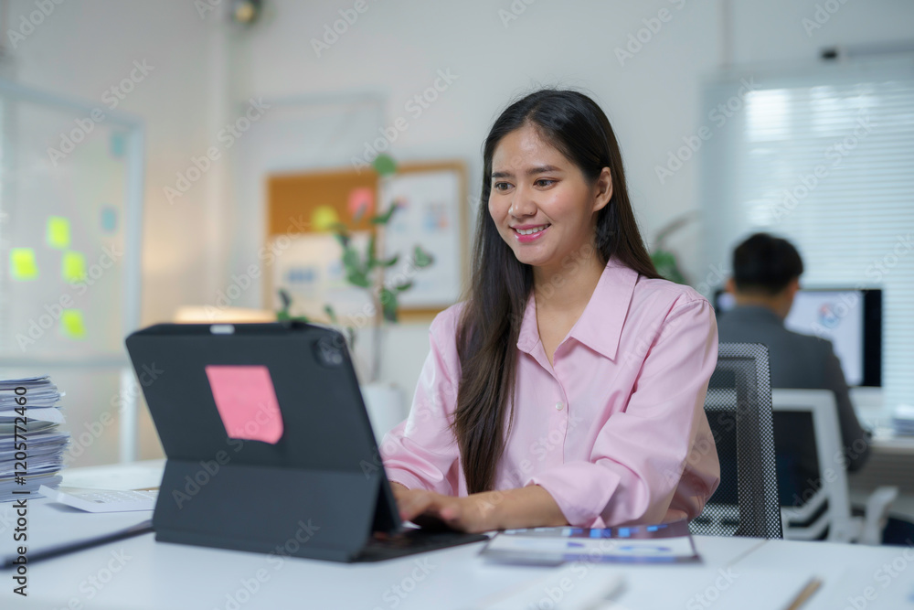 Asian businesswoman smiling while working with tablet at her desk in modern office Asian businesswoman smiling while working with tablet at her desk in modern office