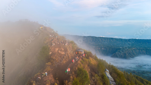 Obraz na płótnie A group of hikers on a foggy mountain peak in Bali, overlooking the stunning Mount Batur volcano. The image highlights the natural beauty and allure of this popular hiking destination w salonie