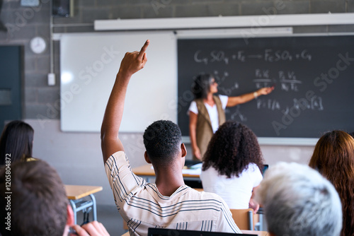 Young group of gen z students attending class at high school. Young black student boy hand raised asking a question to senior female teacher during lecture. Education concept