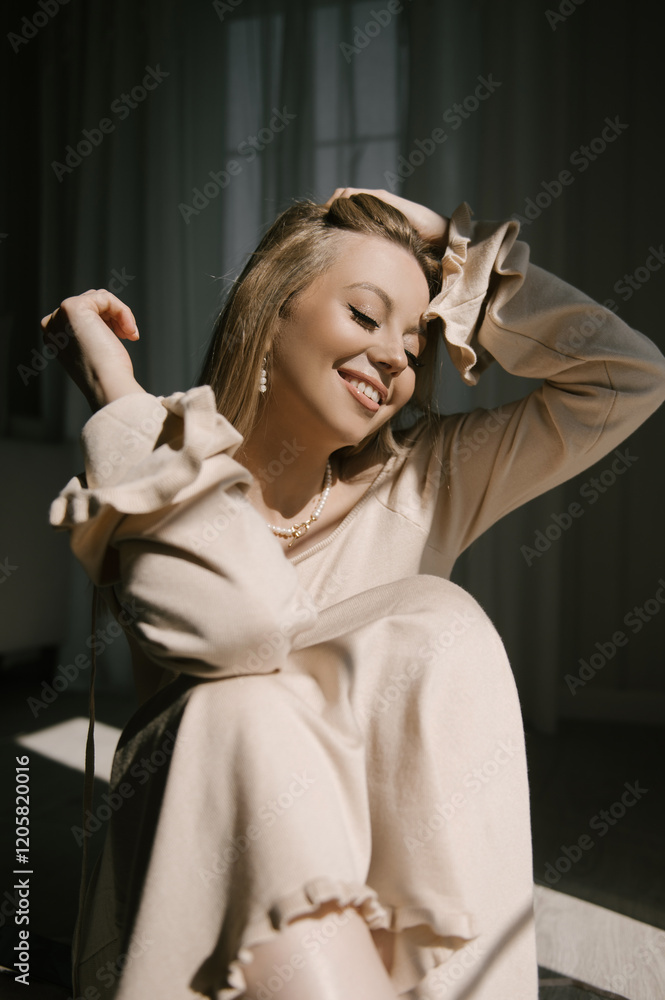 Beautiful blonde woman posing near the window in the sun rays in a beautiful modern stylish beige interior