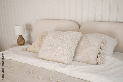 Beautiful light beige interior with soft white bed decorated with pillows in japandi and wawabi sabi style, cozy home concept