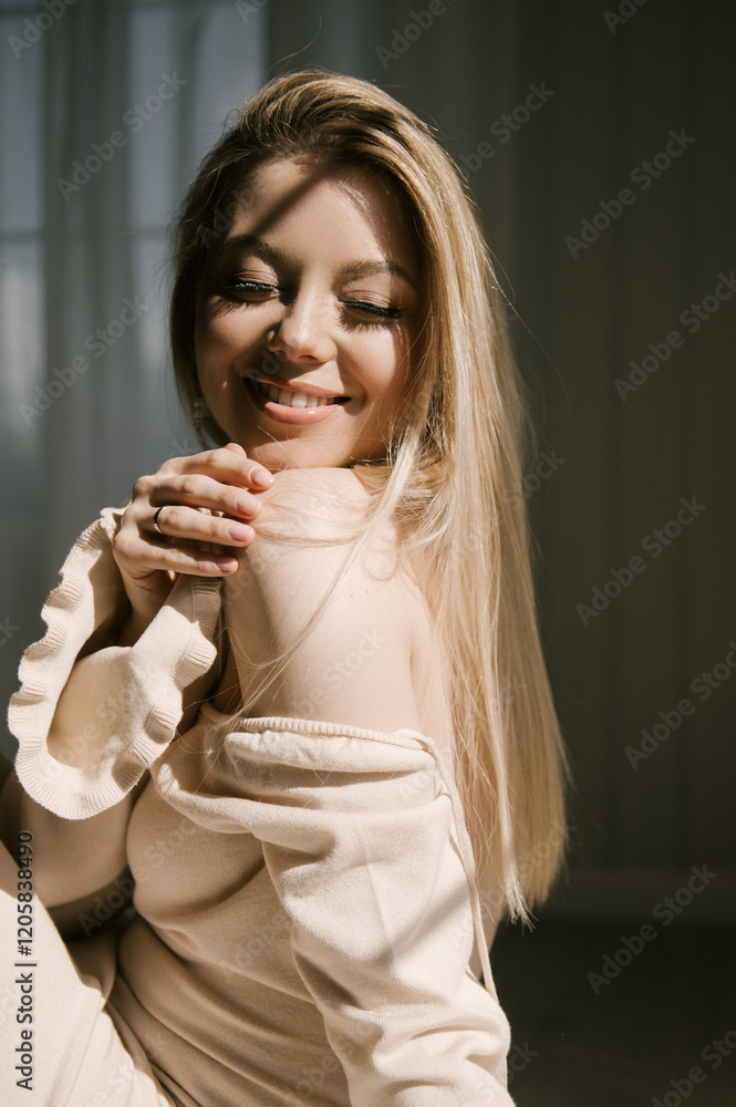 Beautiful blonde woman posing near the window in the sun rays in a beautiful modern stylish beige interior