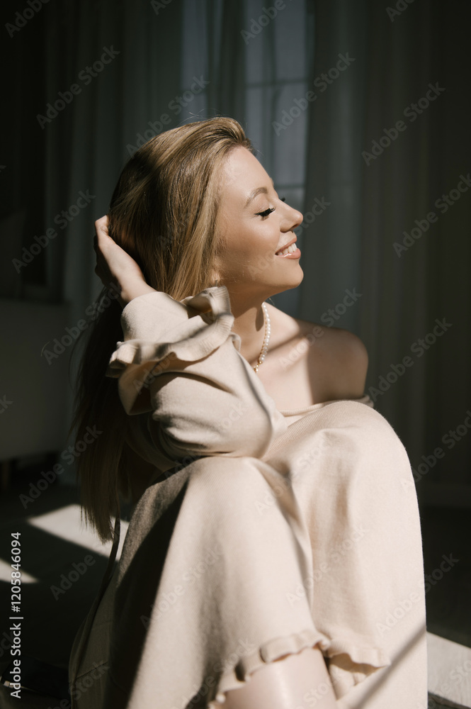 Beautiful blonde woman posing near the window in the sun rays in a beautiful modern stylish beige interior