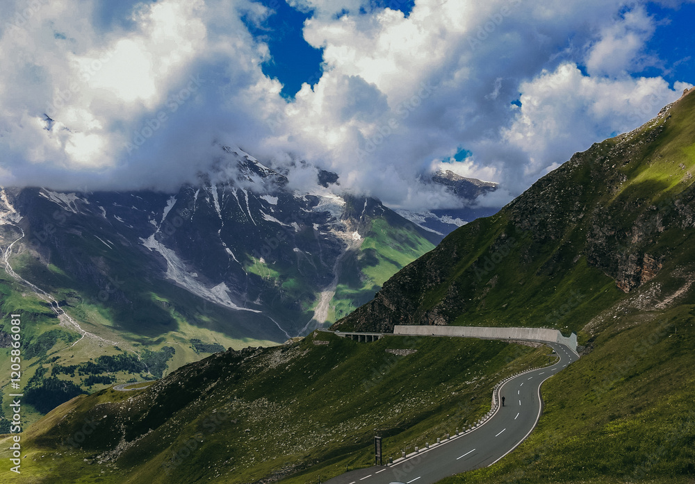 A winding mountain road cuts through lush green hills under a dramatic sky with clouds A winding mountain road cuts through lush green hills under a dramatic sky with clouds
